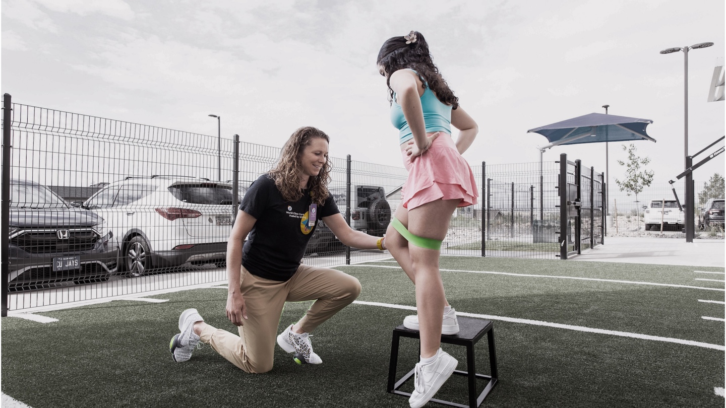 Person in a field examining a patient who is stepping on a stool with a green band around the legs