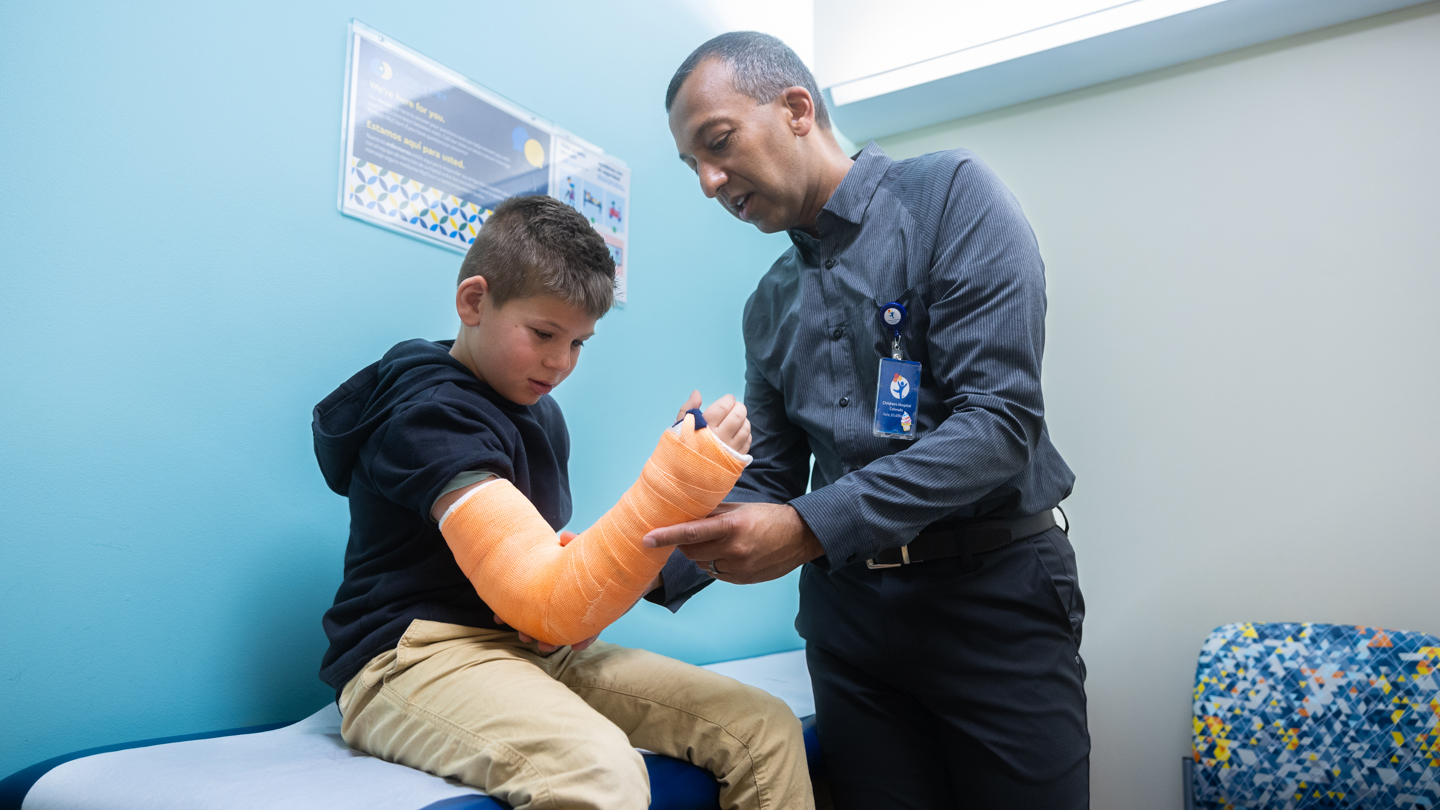 Person examining a patients arm that is in an orange cast 