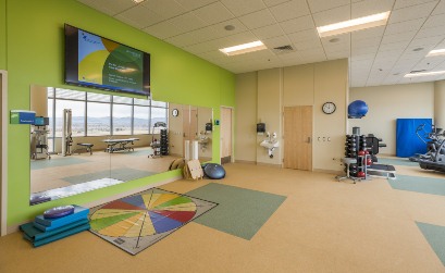 A picture of the sports gym at South Campus showing a stack of weights, balance ball, balance boards, a mirror and a TV hanging above the mirror on a bright green wall.