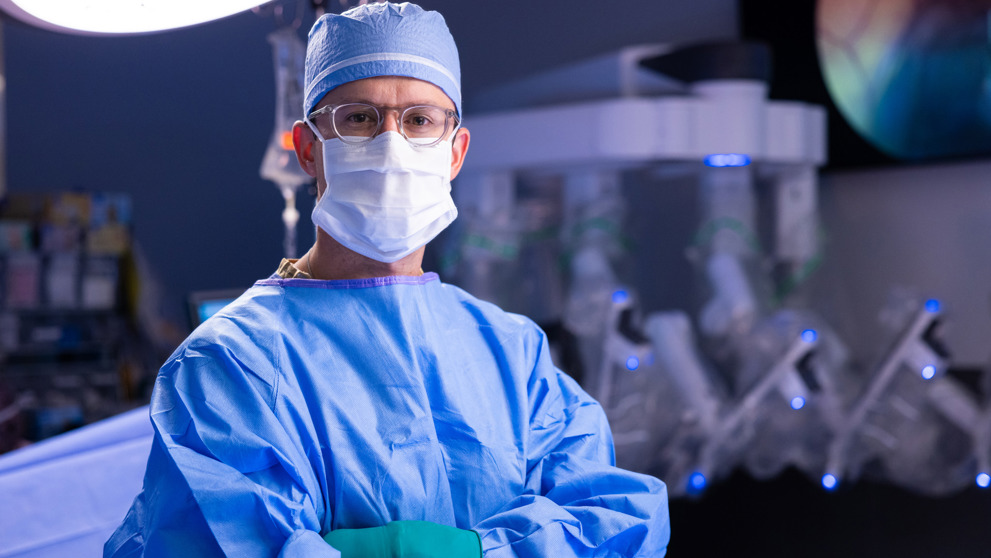 Seurgeon posing for a photo in a surgery room wearing medical gear 