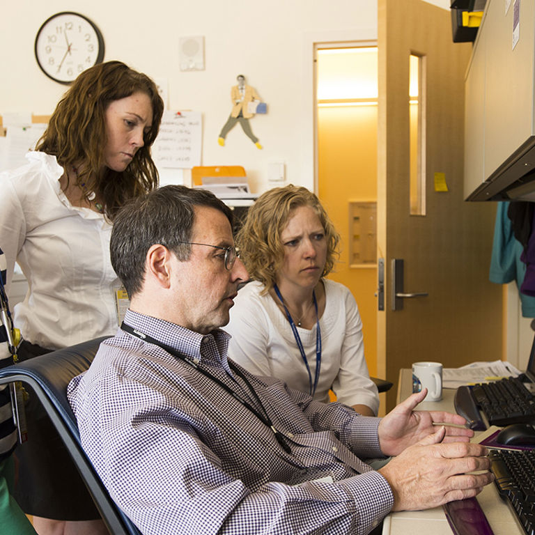 A group of professionals gathers around a computer screen.