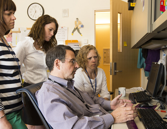 A group of professionals gathers around a computer screen.