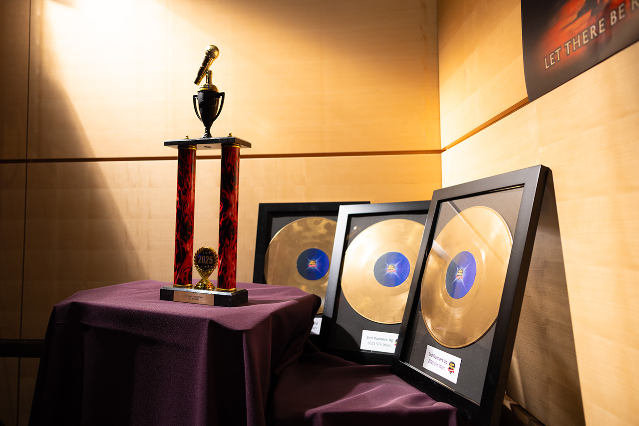 Display table at Sim Wars featuring a tall trophy with a microphone topper alongside framed gold record-style awards