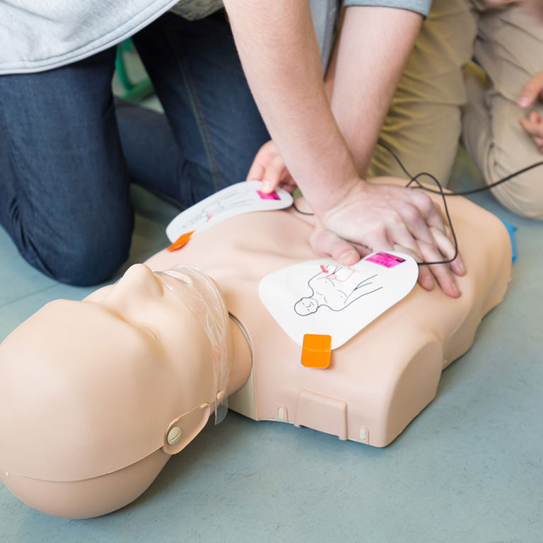 Students and staff participating in a cardiac emergency response drill on a playground.