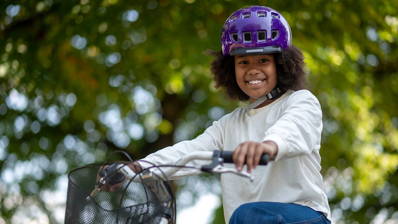 Girl smiling in purple helmet riding a bike outside 