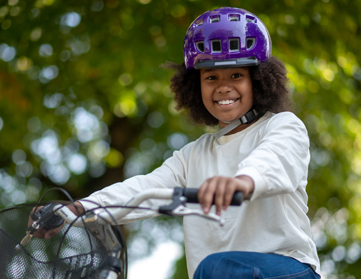 Girl smiling in purple helmet riding a bike outside 