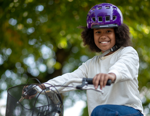 Girl smiling in purple helmet riding a bike outside 