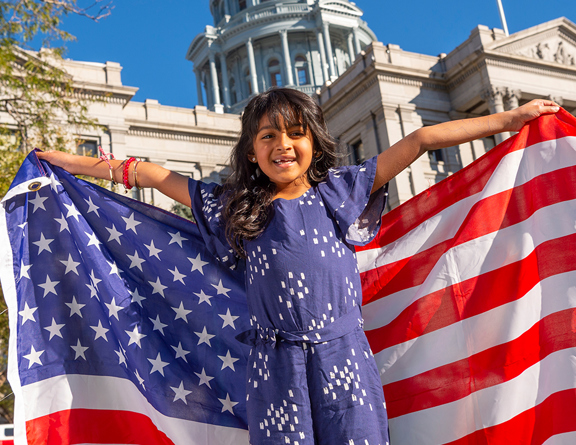 Child holding an American flag in front of building 