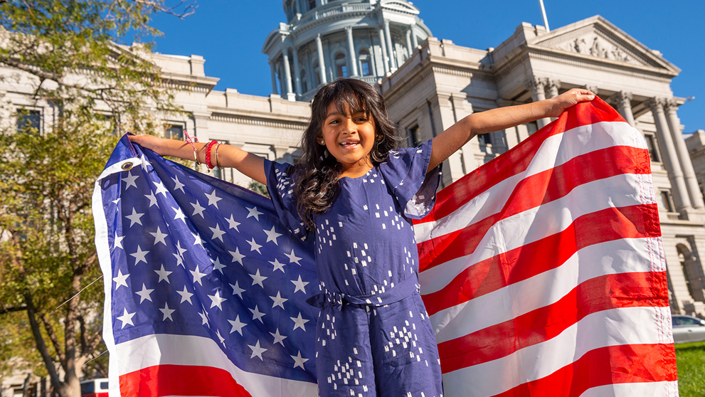 Child holding an American flag in front of building 