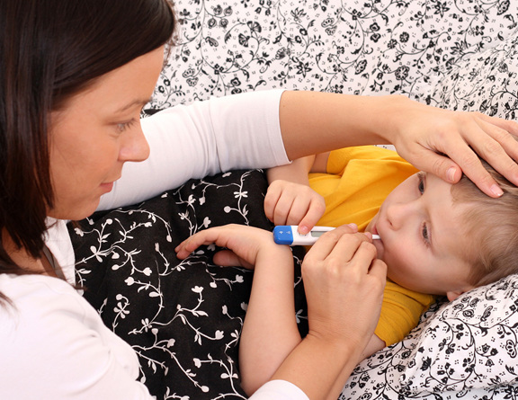 A parent places their hand on the forehead of a sick child while taking their temperature with a thermometer.