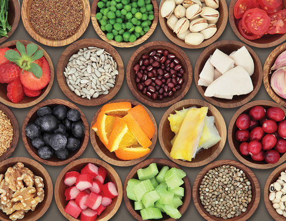 Various healthy foods such as oranges, blueberries, celery, and black beans in brown wooden bowls.