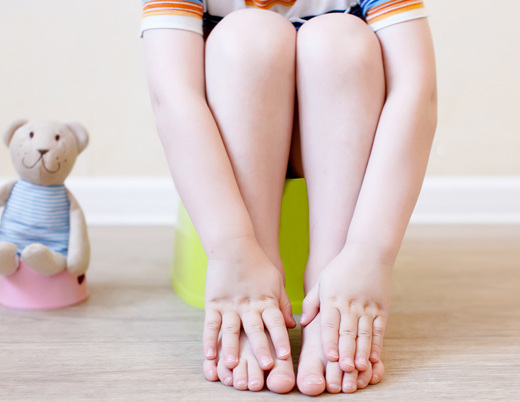 A toddler sits on a training potty next to a stuffed teddy sitting on a toy potty.