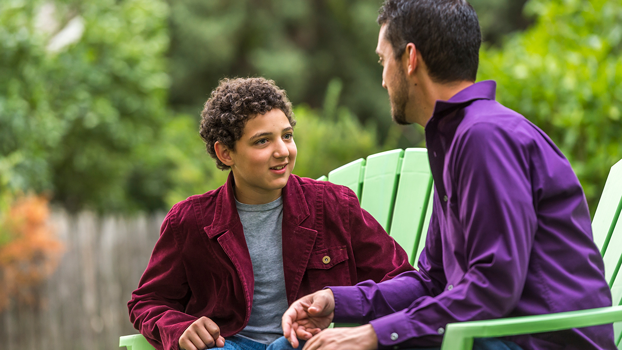 A father and son sit outside and talk about mental health.