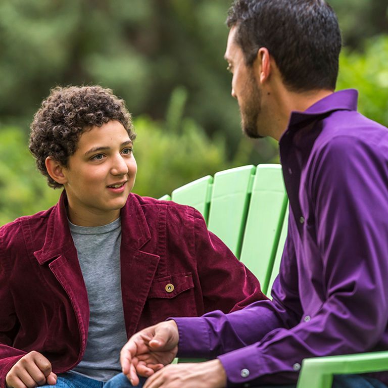 A father and son sit outside and talk about mental health.