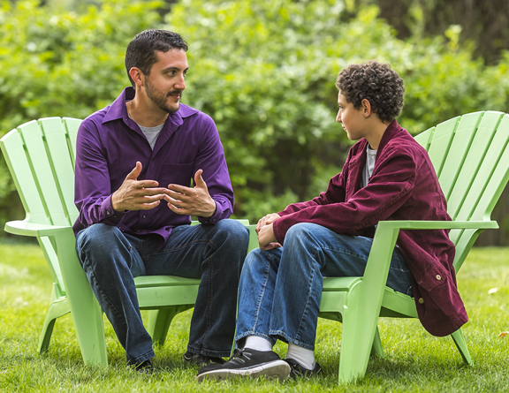 A father is having a conversation with his son outdoors sitting in lawn chairs.
