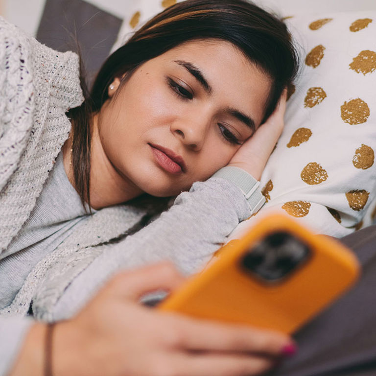 A teenage girl lies in bed while looking at her phone