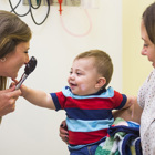 A healthcare provider examines a smiling baby during a well-child visit at the pediatrician.
