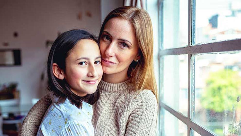 A school-aged girl embraces her mother at home.