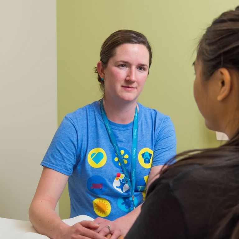A mental health provider at Children's Hospital Colorado sits and listens to a teenage child in a patient room.
