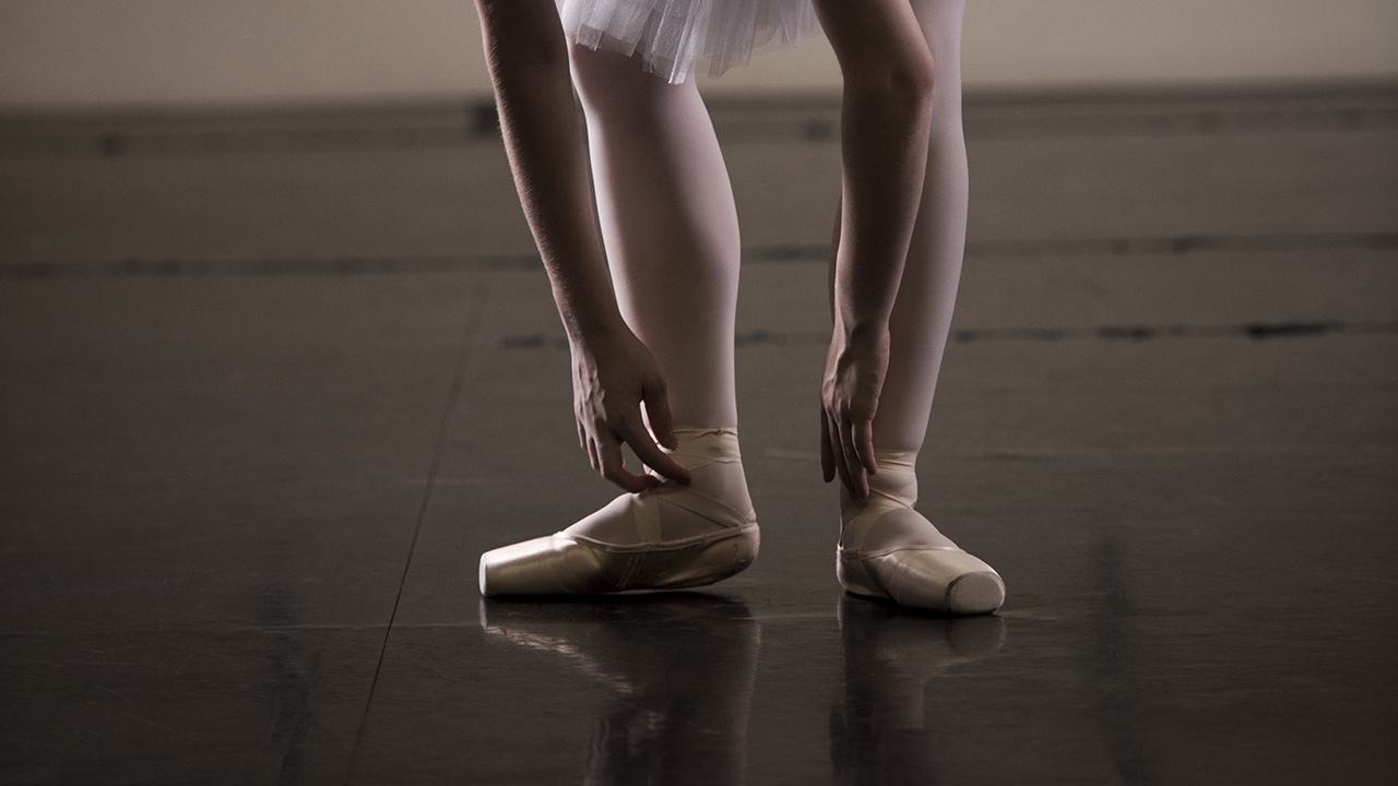 Dancer bending over to fix her pointe shoes