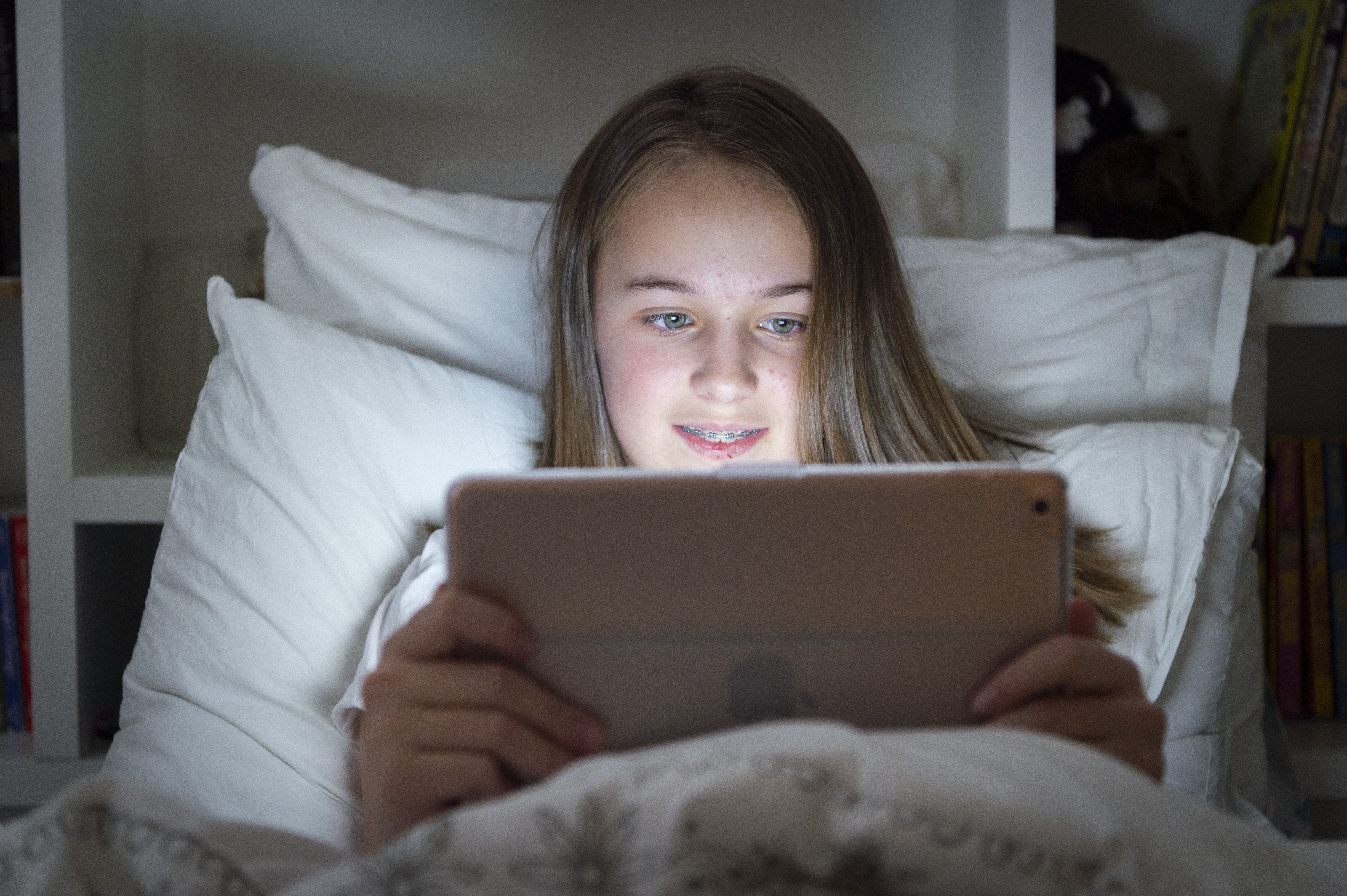 Teen girl looks at tablet at night in bed.
