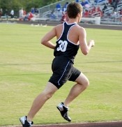 A teenage boy in a black uniform runs on a track.