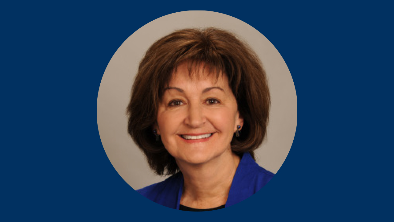 A woman with short brown hair and a blue shirt smiles at the camera. Her face is in a gray circle over a dark blue background.
