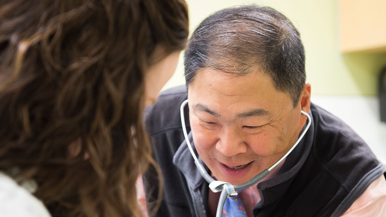 Dr. Furuta at Children’s Hospital Colorado uses a stethoscope with a young patient sitting on her mother’s lap.