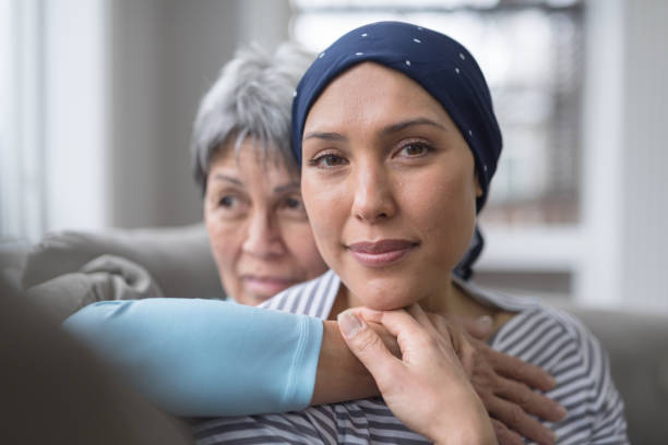 A young woman with a head scarf sits with an older woman behind her with her hand around her shoulder