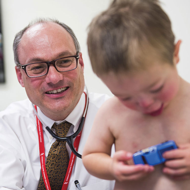Dr. Dunbar Ivy Listens to a toddler's heart while the child plays with a toy car.