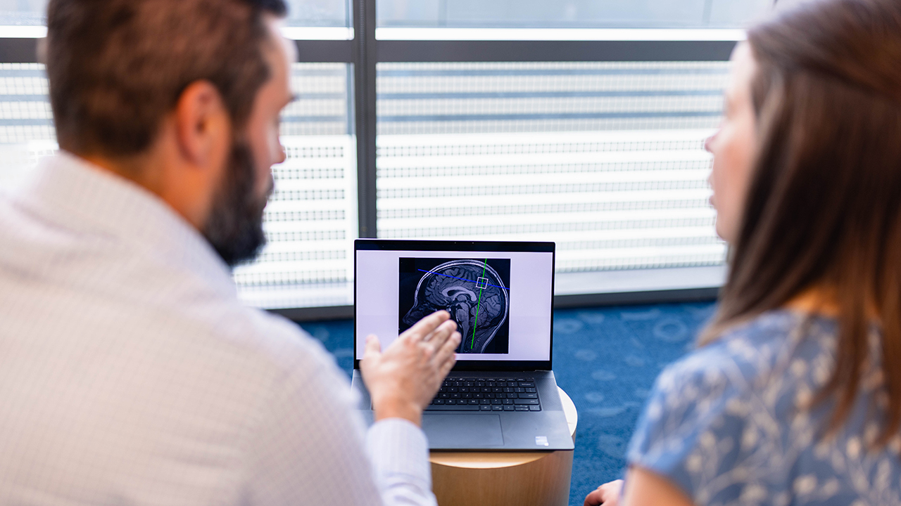 Two researchers at Children’s Colorado talk to each other and look at a laptop screen with brain scan.