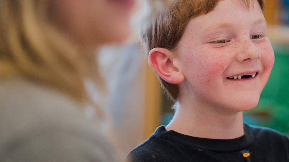 A close-up of a kid with freckles and red hair smiling with his two front teeth missing.